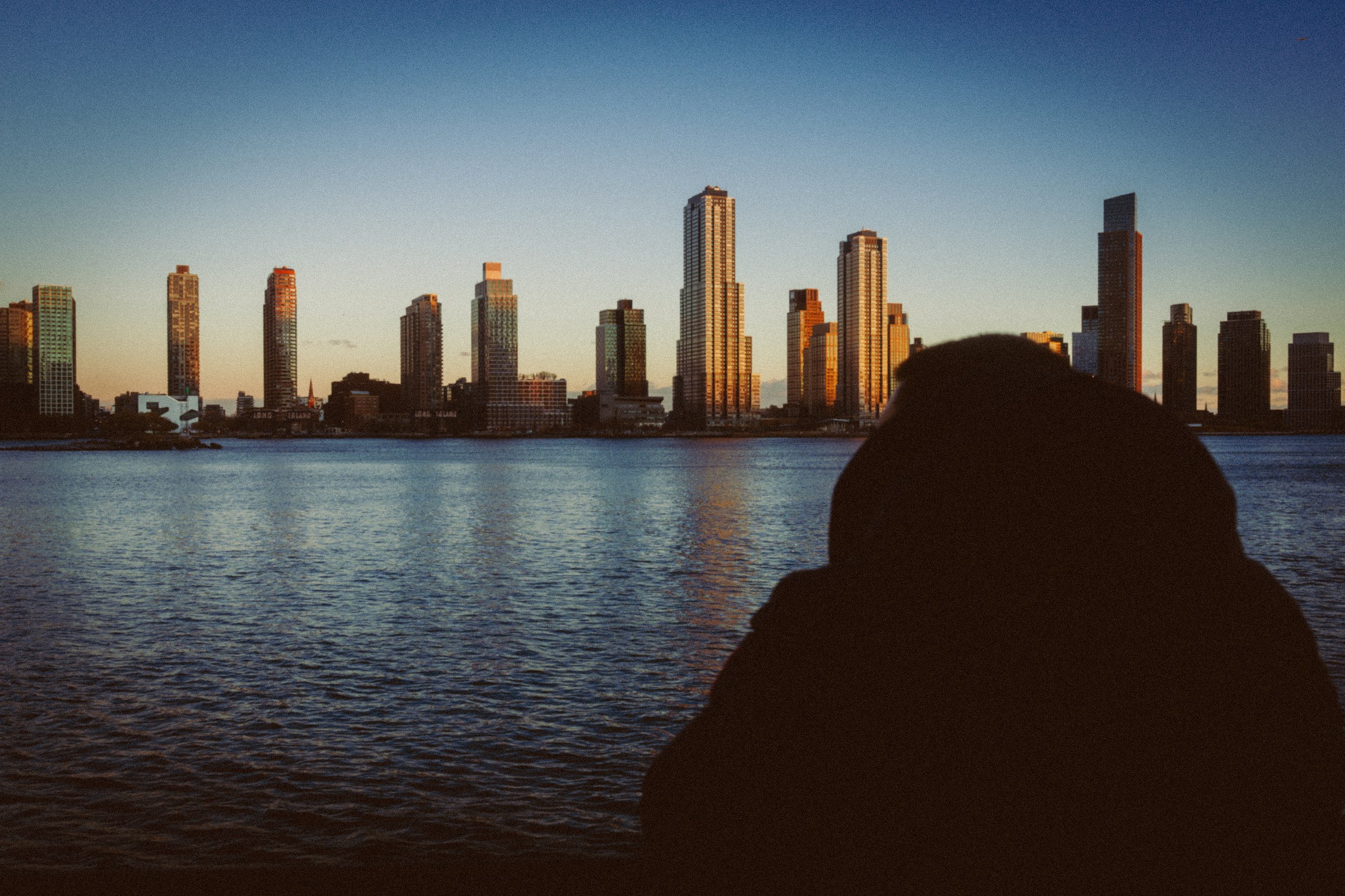 Silhouette of person overlooking city skyline at sunset.
